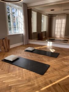 Rolig yogamåtte med pude i et lyst, roligt træningsrum med store vinduer og spejl. Perfekt til afsla.
