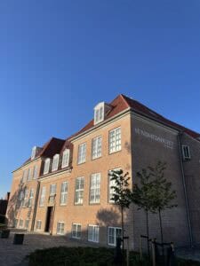 Højt bygning med rødt tag og mange vinduer, Sundhedshuset i centrum. Smuk solrig dag med blå himmel.